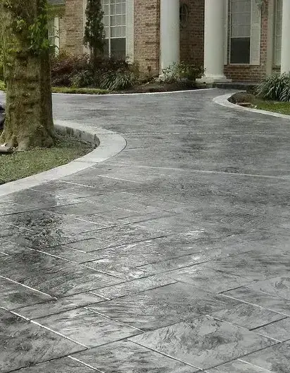 Worker applying stamp mats to fresh concrete creating a decorative stone pattern.